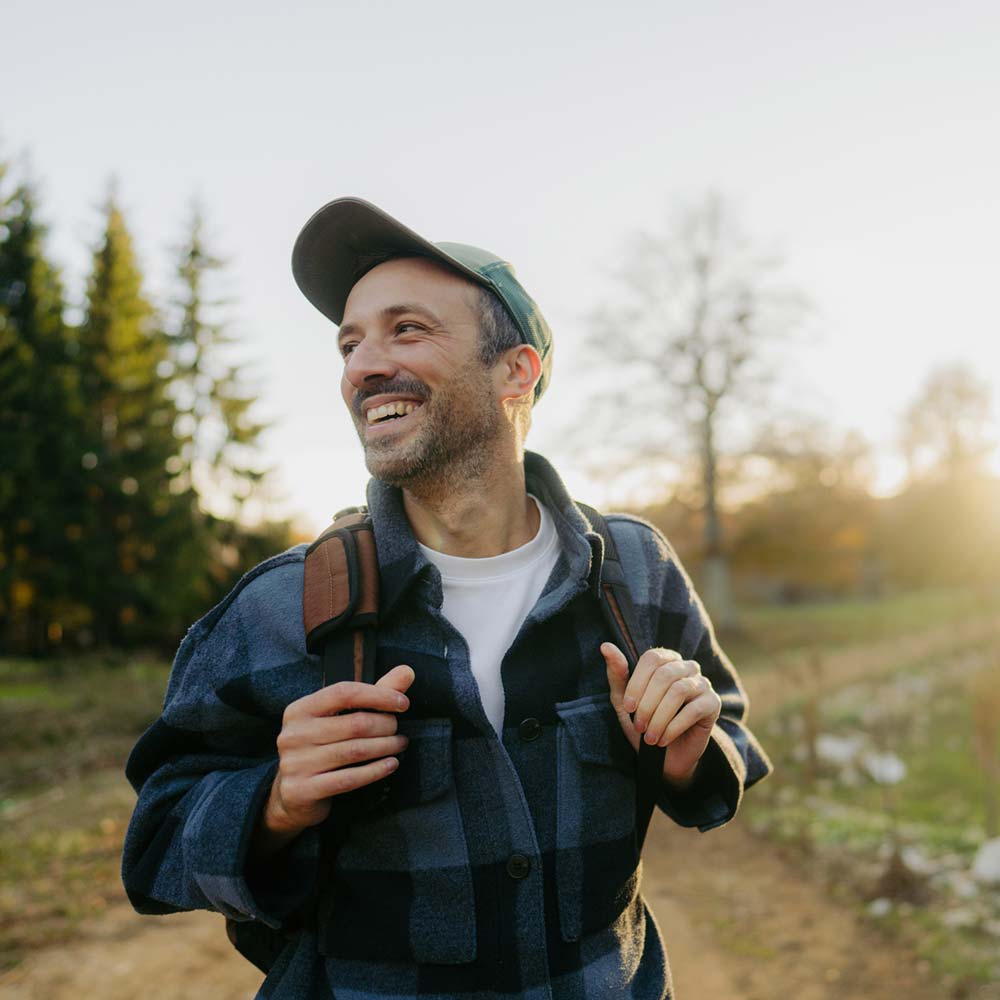 a man in a flannel shirt and a backpack smiles and hikes down the trail