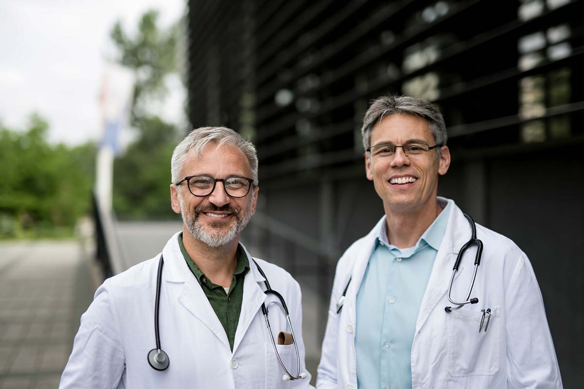 two male doctors stand and smile at the camera