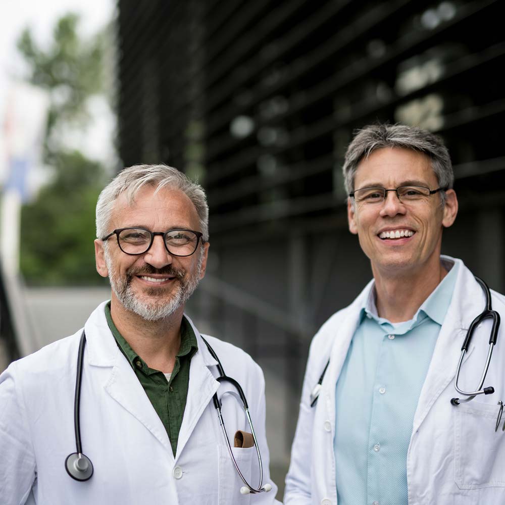 two male doctors stand and smile at the camera