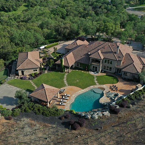 drone shot of a large mansion with a pool, yard, and golf area surrounded by green trees