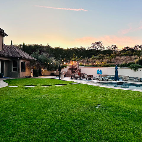 a well groomed green yard with a pool and string patio lights