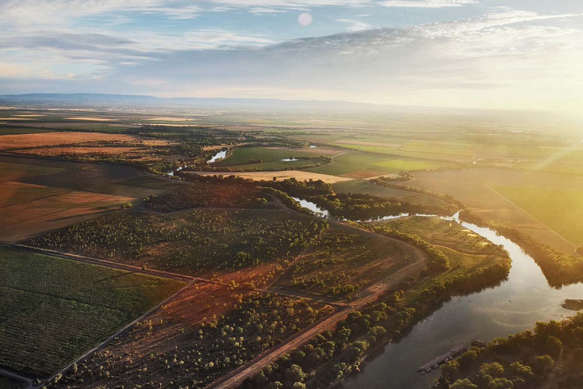 an evening sunset casts its warm glow over a patchwork of farm fields and a river winding its way through the land