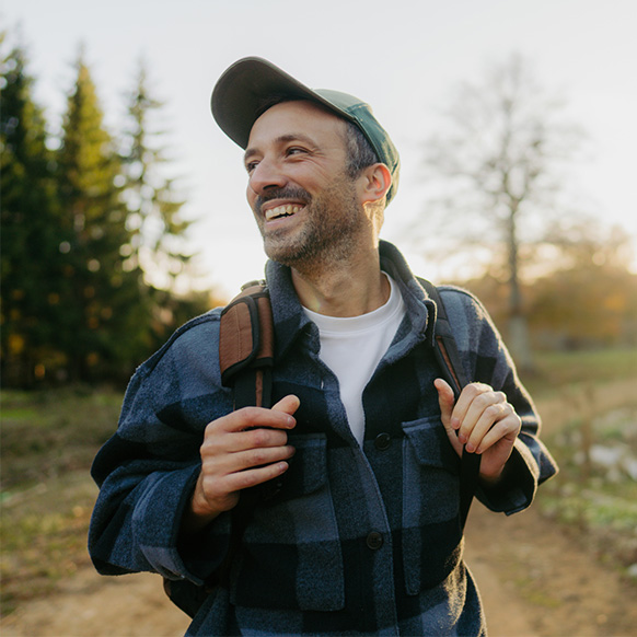 a man in a flannel shirt and a backpack smiles and hikes down the trail