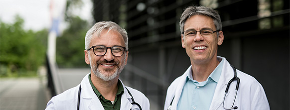 two male doctors stand and smile at the camera