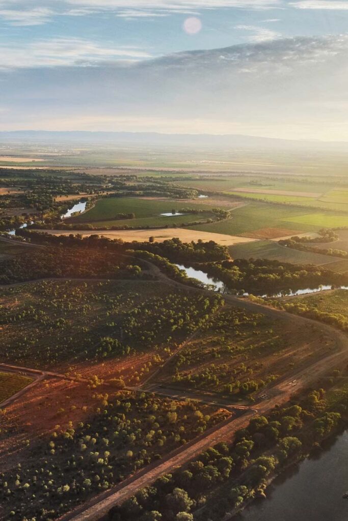 an evening sunset casts its warm glow over a patchwork of farm fields and a river winding its way through the land