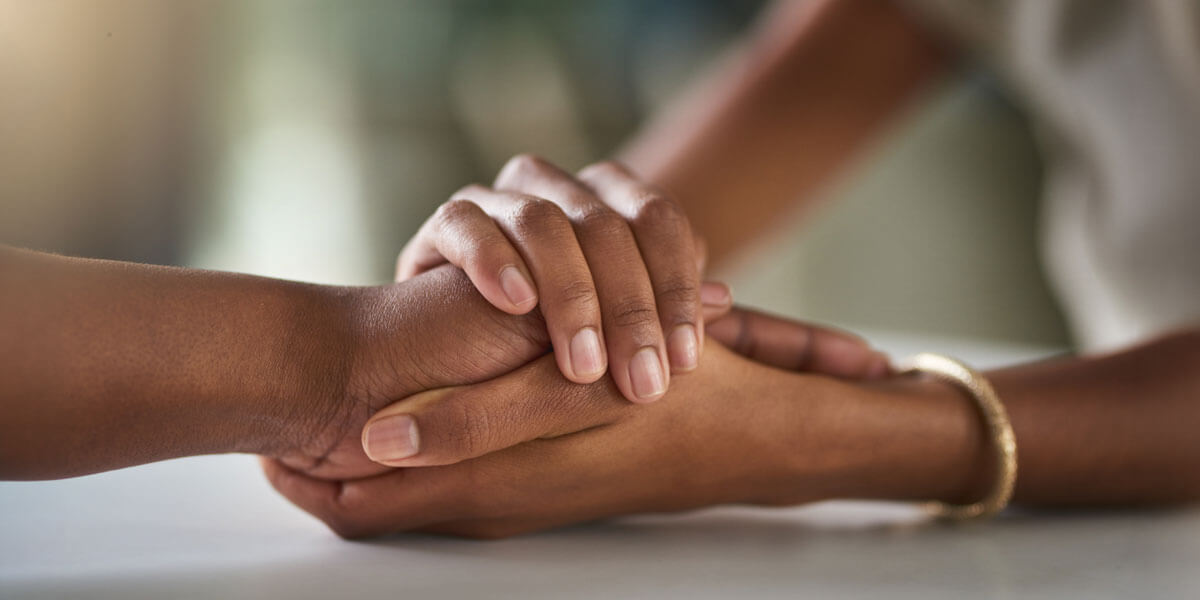 Close-up of two people's hands clasped together in a gesture of comfort and support.
