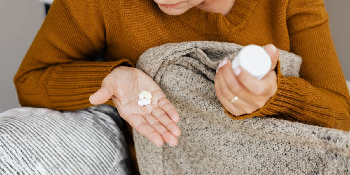 Woman in a sweater holding pills in one hand and a medication bottle in the other.