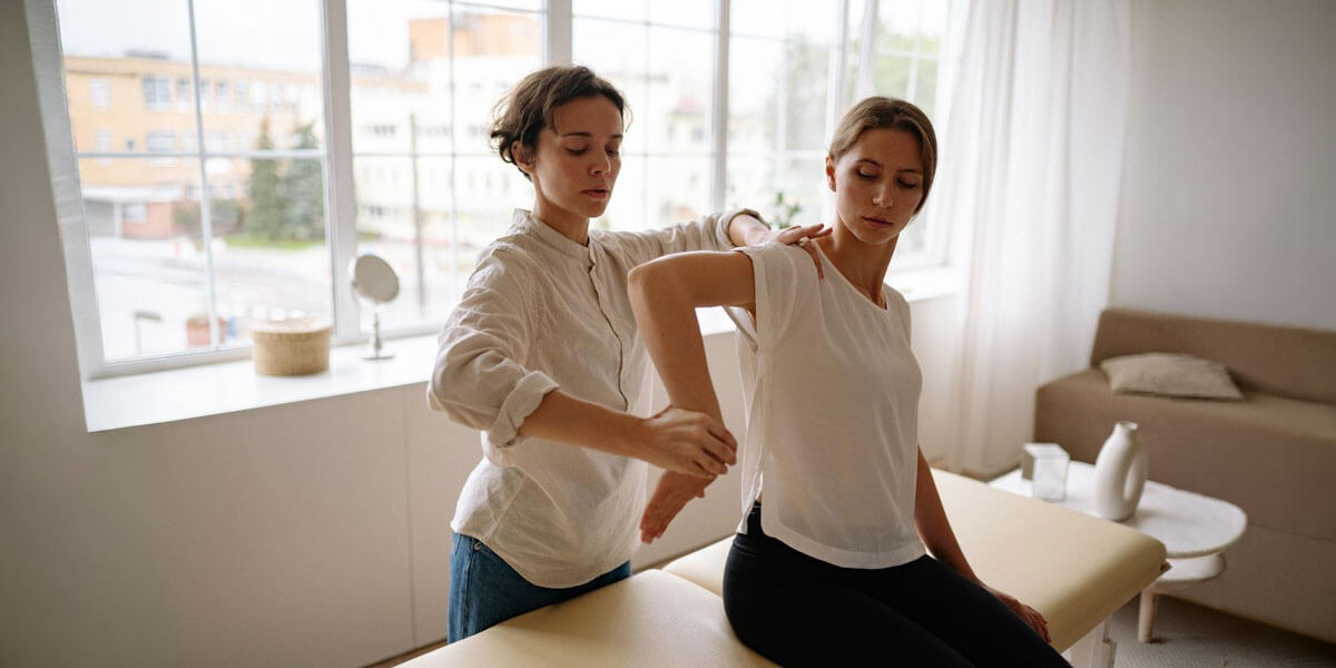 A physical therapist helps a woman stretch her arm during a rehabilitation session.