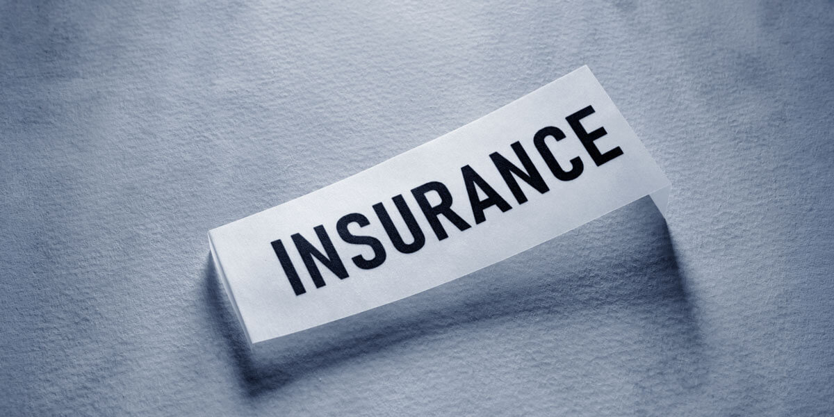 A torn strip of paper with the word "Insurance" printed on it rests on a textured blue-gray fabric background.