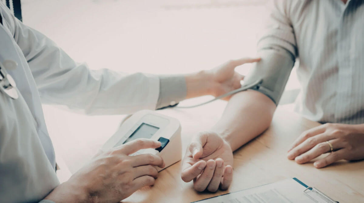 A healthcare professional checking a patient’s blood pressure with a monitor in a clinical setting.